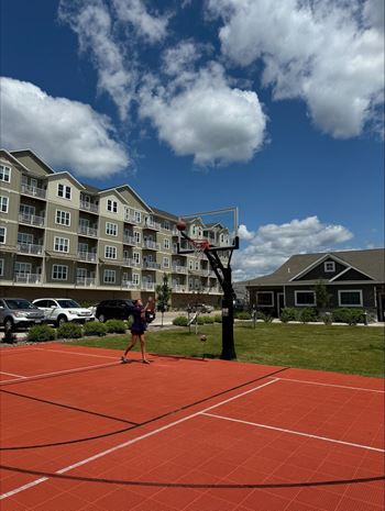 a woman playing basketball on a red court in front of an apartment building